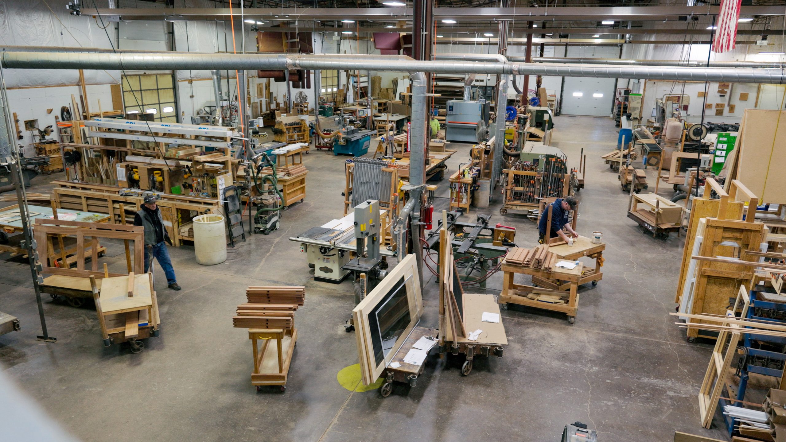 Wide view of a custom door workshop floor, with workbenches, saws and part-built door frames on rolling carts.